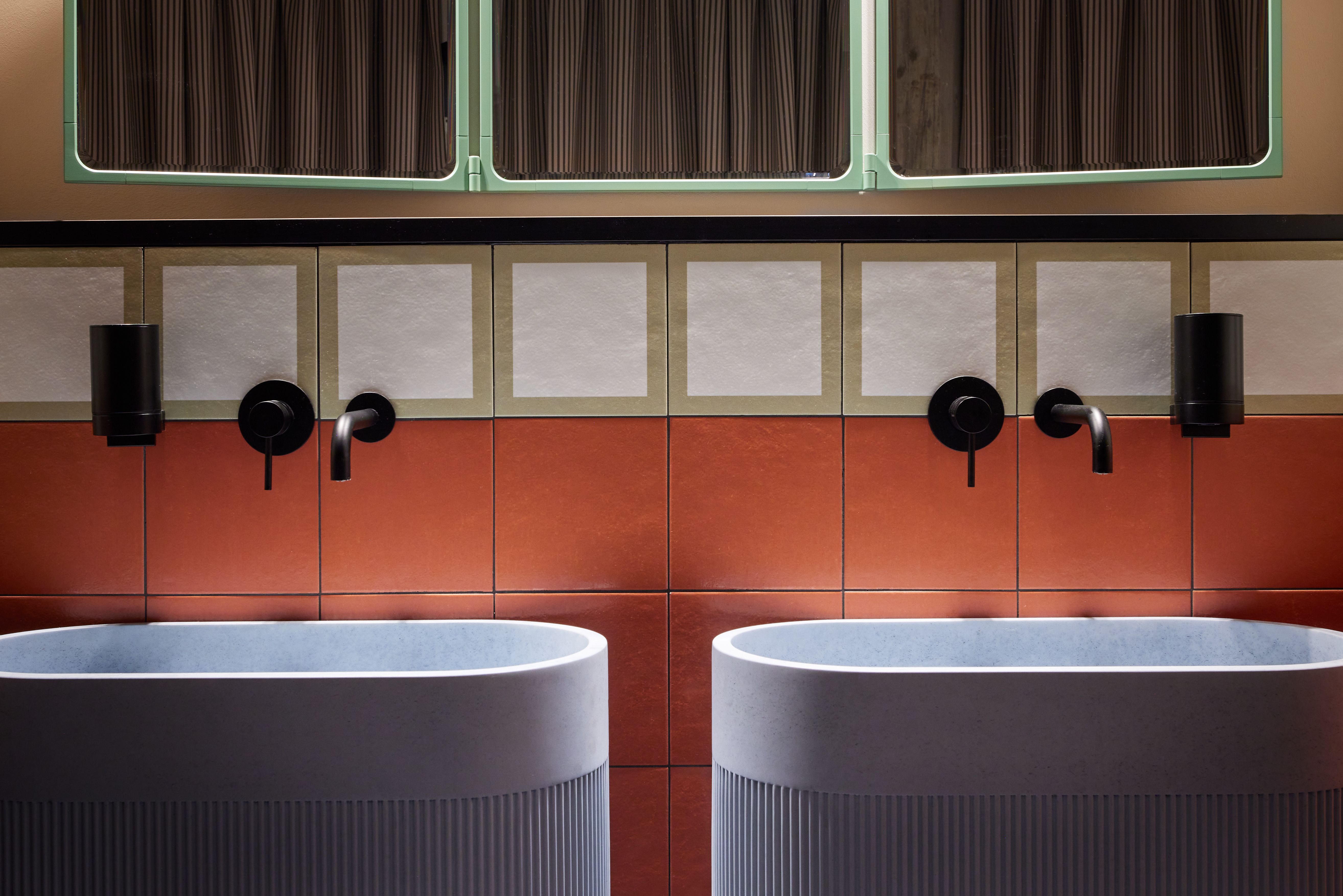 Die farblich strukturierte Waschtischzone mit schwarz lackierten Sanitäraccessoires, kontrastreicher Kachelrahmung und präziser Lichtführung wurde im Turbinenhaus Kolbermoor – Brasserie von Stephanie Thatenhorst designt.