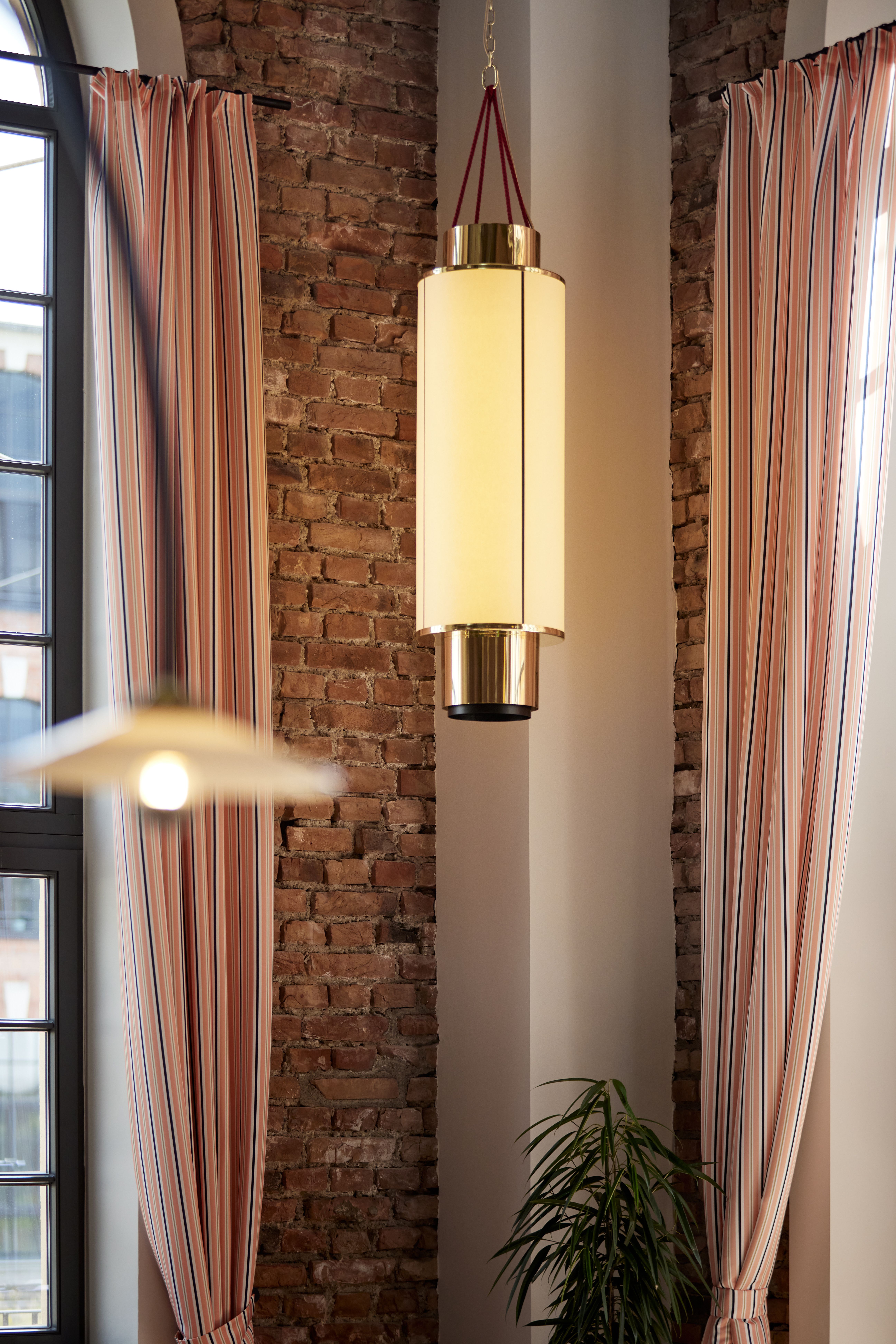 Lichtskulptur im Zylinderkorpus mit Messingapplikation vor freigelegtem Backsteinmauerwerk, designt von Stephanie Thatenhorst für das Turbinenhaus Kolbermoor – Brasserie.