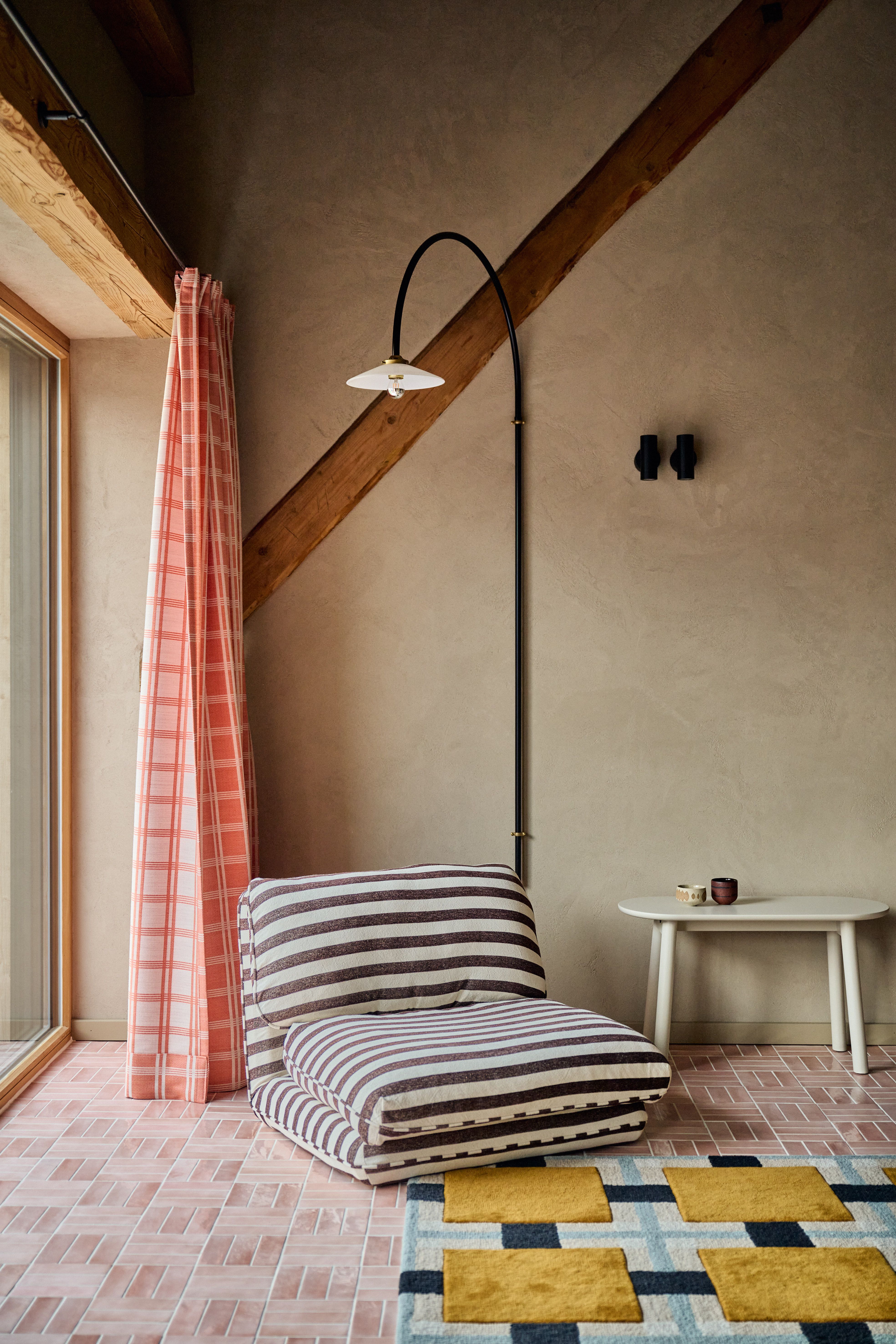 Lounge-Nische mit grafisch gestreiftem Bodensitzmöbel, rosa Karovorhang und minimalistischer Bogenleuchte im Contemporary Mountain Style.