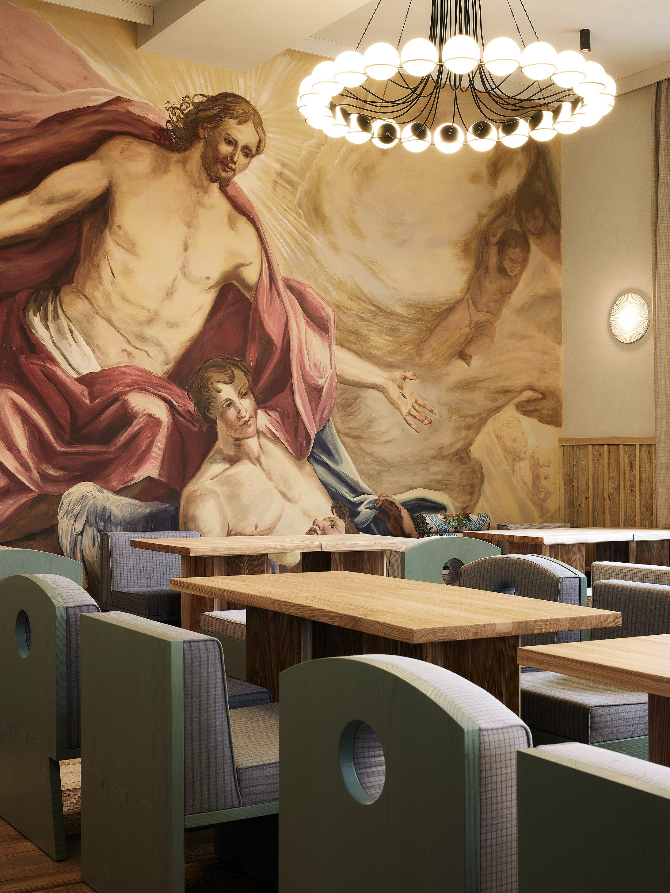 Wandfresko und markanter Kronleuchter setzen im Gastraum einen starken gestalterischen Akzent und schaffen eine ikonische Atmosphäre.