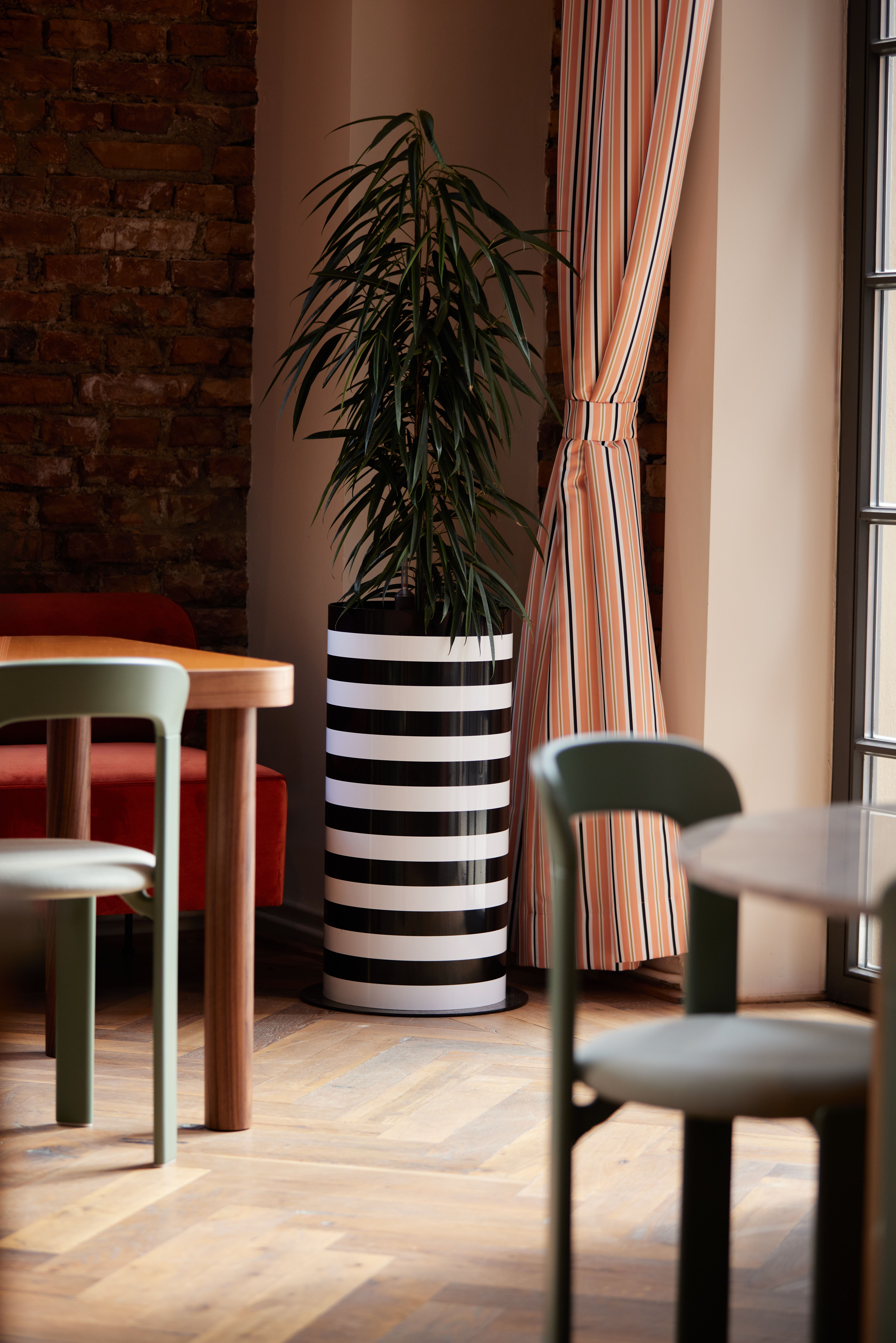 Vertikale Statement-Pflanzenvase im monochromen Stripe-Design als Zonierungselement, kuratiert von Stephanie Thatenhorst für das Turbinenhaus Kolbermoor – Brasserie.