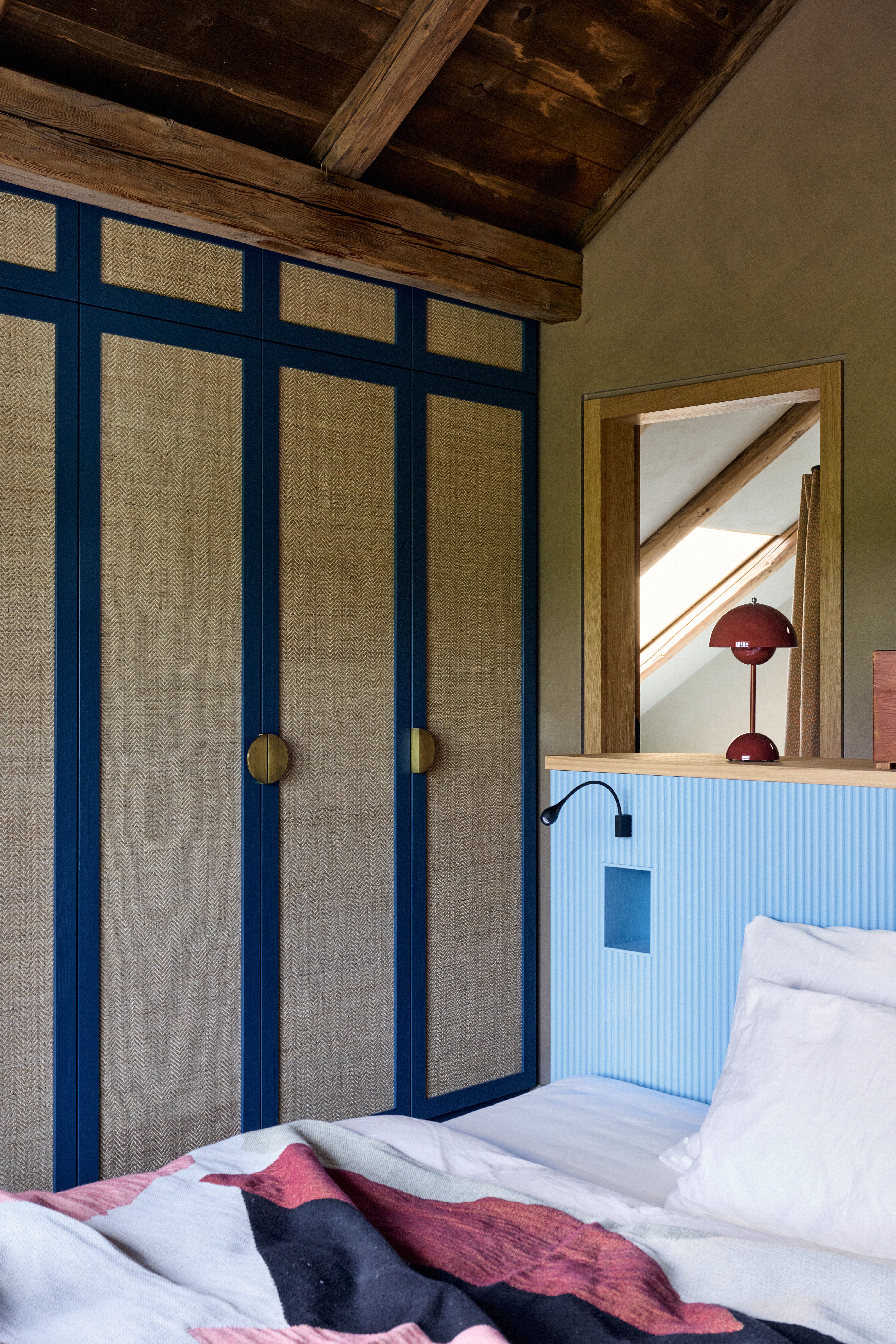 Ruhiger Schlafraum mit intensiver Blau-Holz-Konsole, gewebten Türfronten und ikonischer Tischleuchte als farblichem Akzent.