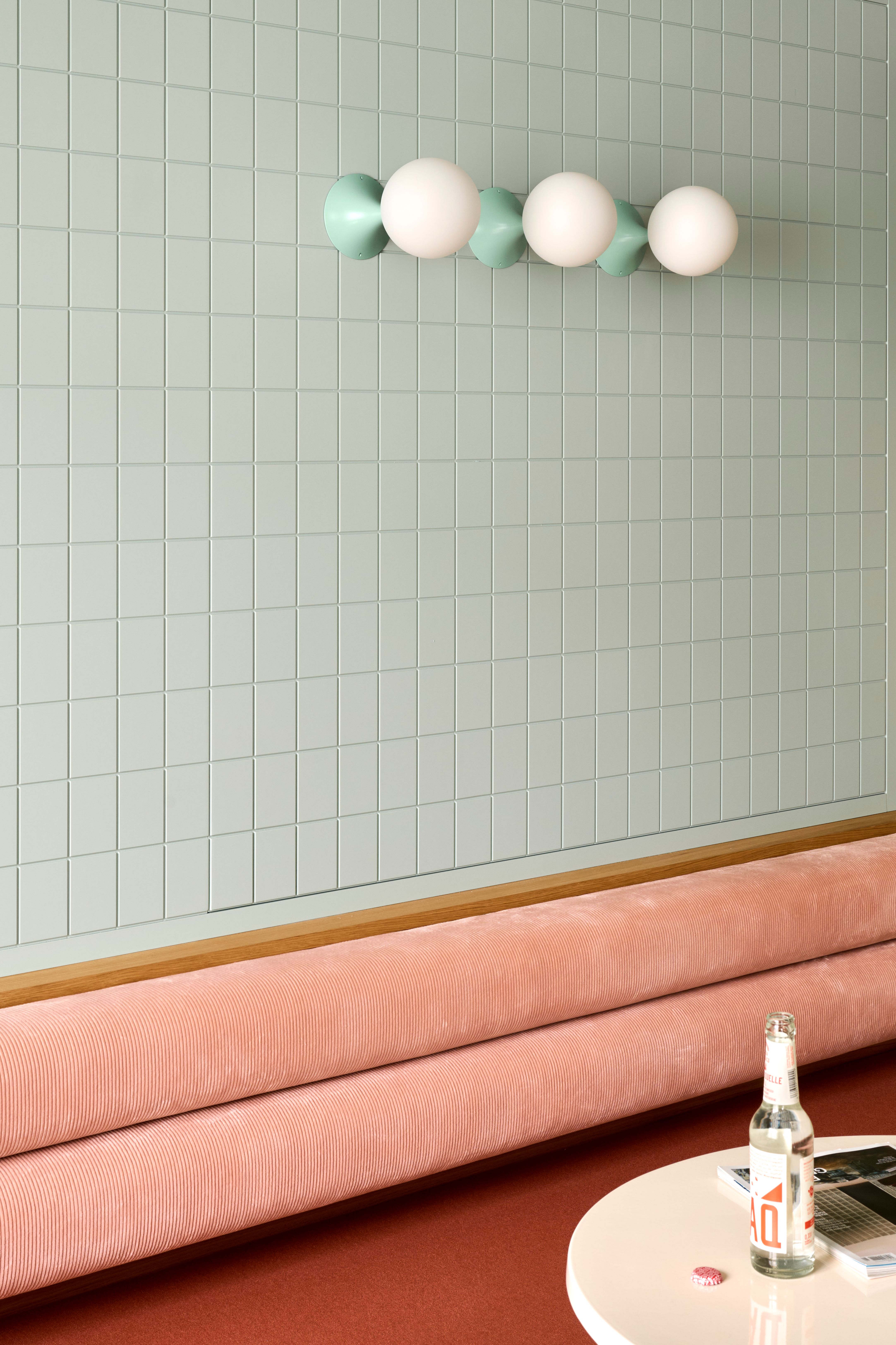 Eine pastellfarbene Wand mit grafischer Beleuchtung und textiler Sitzfläche vermittelt zeitlose Klarheit im Interior-Design von Stephanie Thatenhorst.