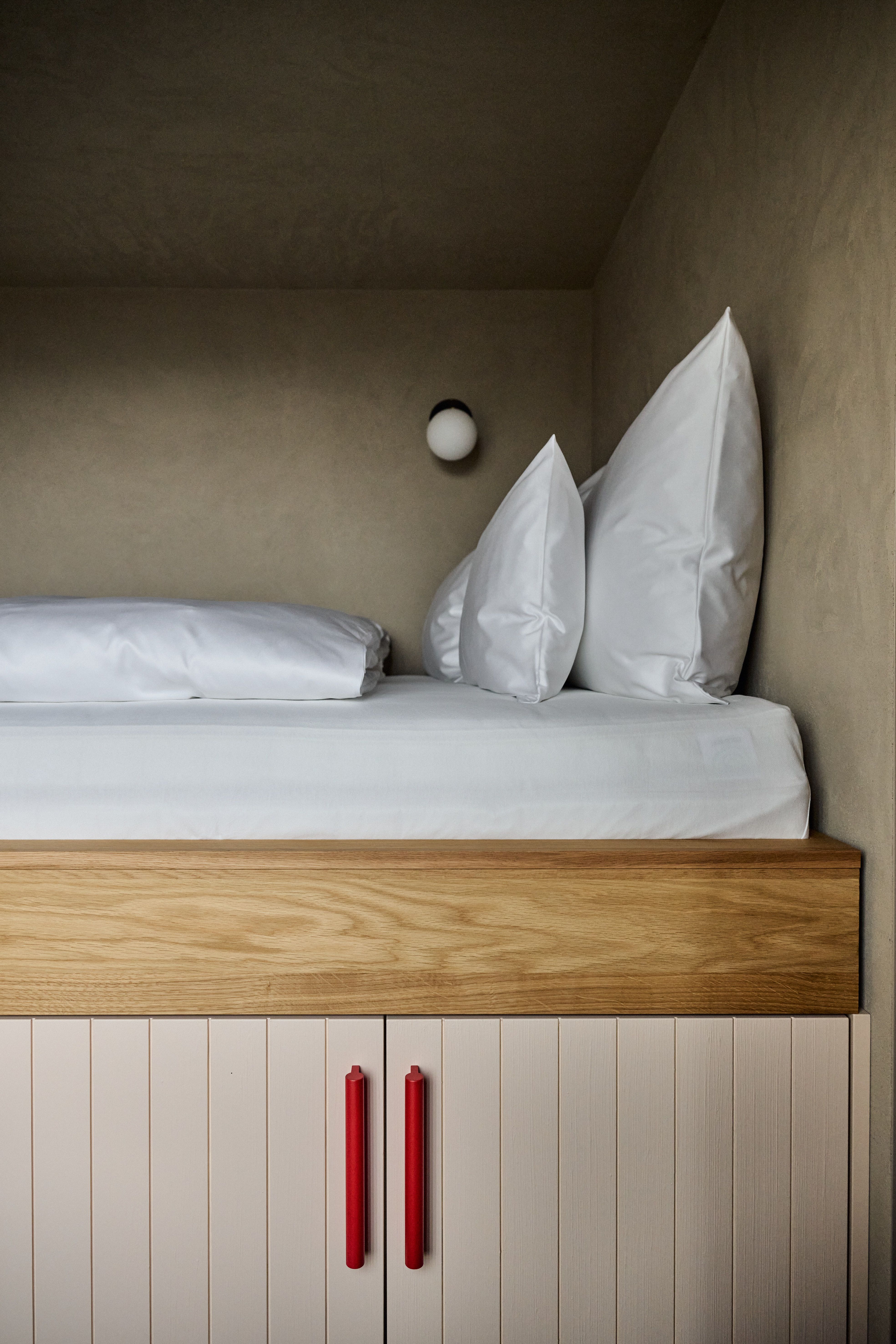 Kompakter Schlafbereich mit maßgefertigtem Stauraum, naturbelassener Holzfront und modernem Leuchtkörper – umgesetzt von Stephanie Thatenhorst.