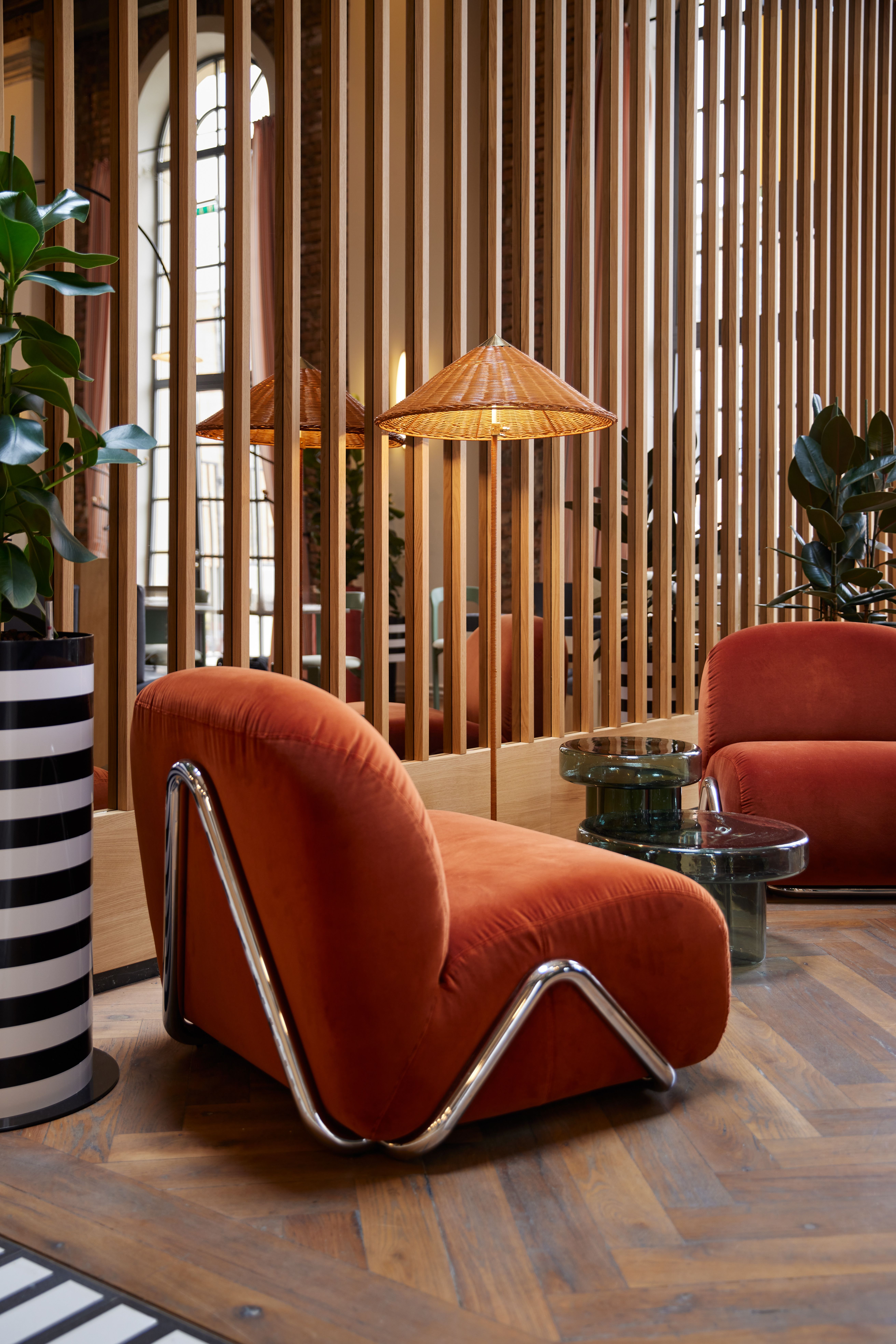 Die Lounge-Ensembleinszenierung mit chromrohrgefassten Velours-Sesseln, strukturellem Holzlamellen-Grid und ikonischem Glas-Tischobjekt wurde im Turbinenhaus Kolbermoor – Brasserie von Stephanie Thatenhorst designt.