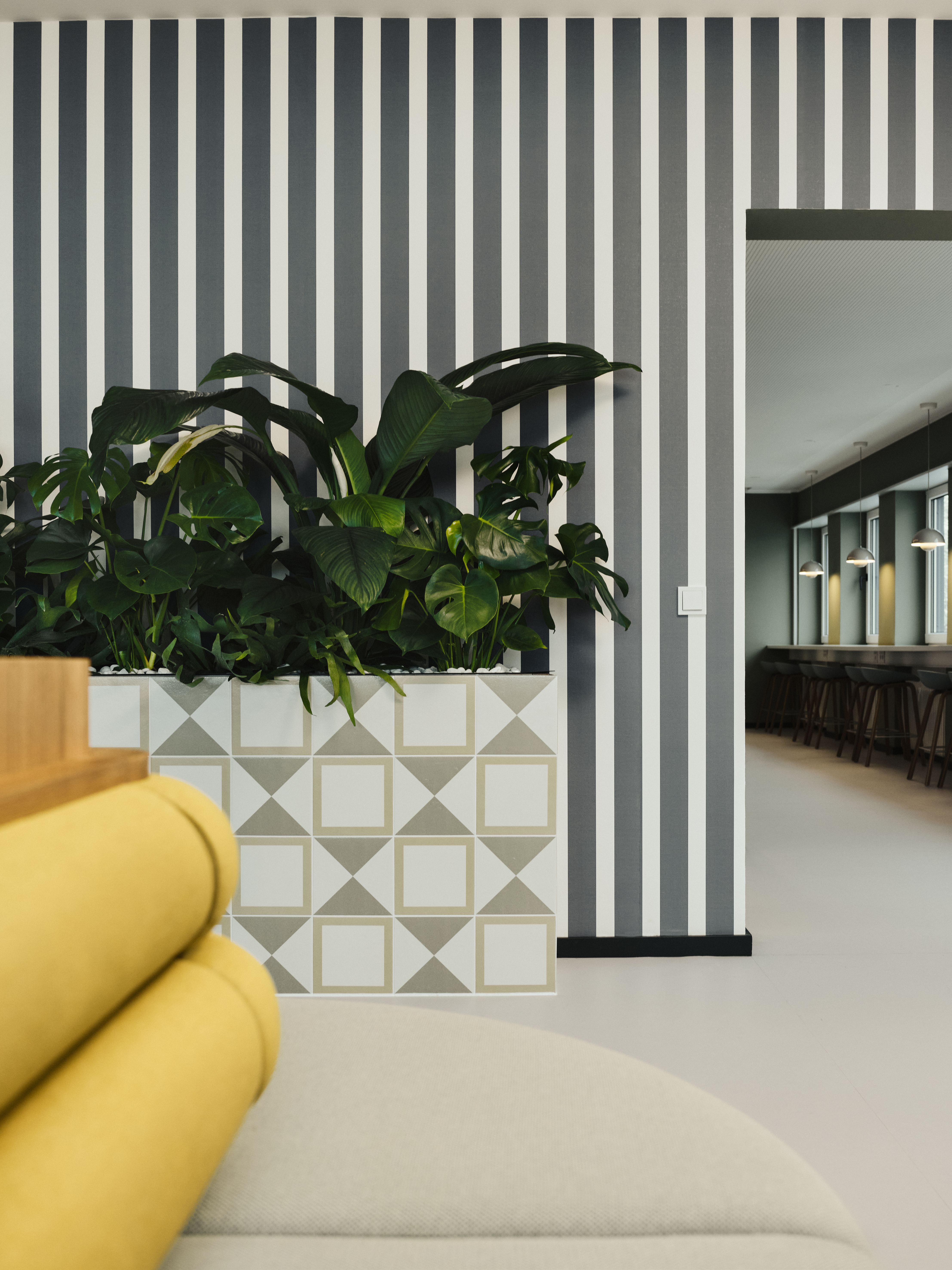 Vertikale Streifenwände, strukturierte Fliesen und üppige Pflanzeninseln sorgen für ein lebendiges Raumgefüge, designed by Stephanie Thatenhorst.