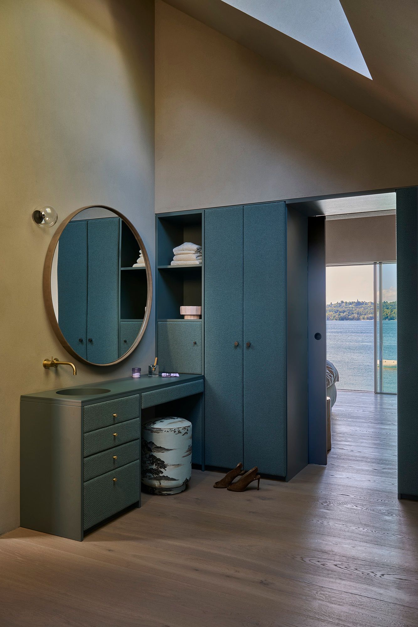Stilvolles Ankleide-Design von Stephanie Thatenhorst mit maßgefertigten Einbauten, rundem Spiegel und Blick auf den See.