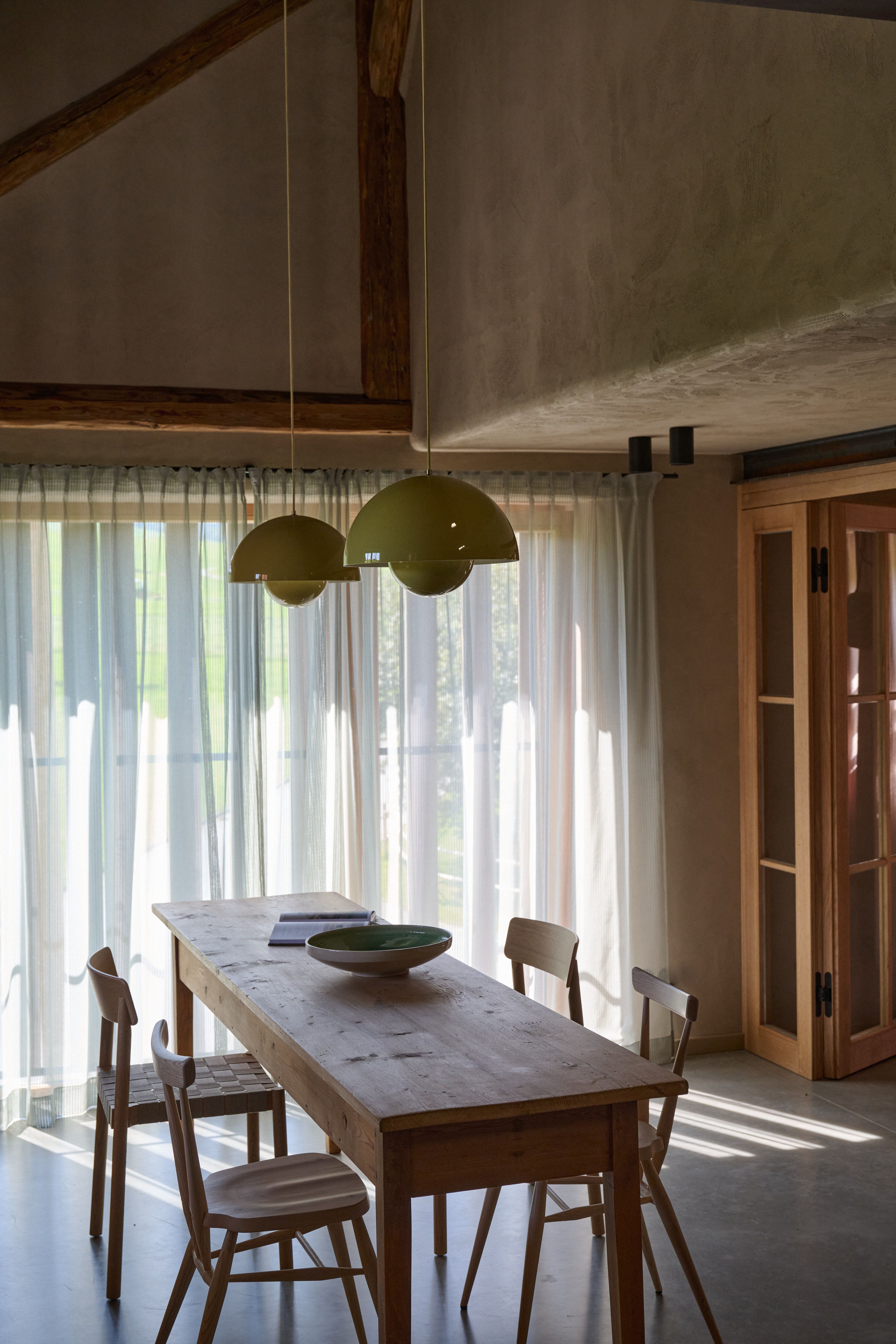 Puristisch gestalteter Essbereich mit charakterstarken Holzmöbeln, hellen Vorhängen und ikonischen Pendelleuchten in Soft-Gelb.