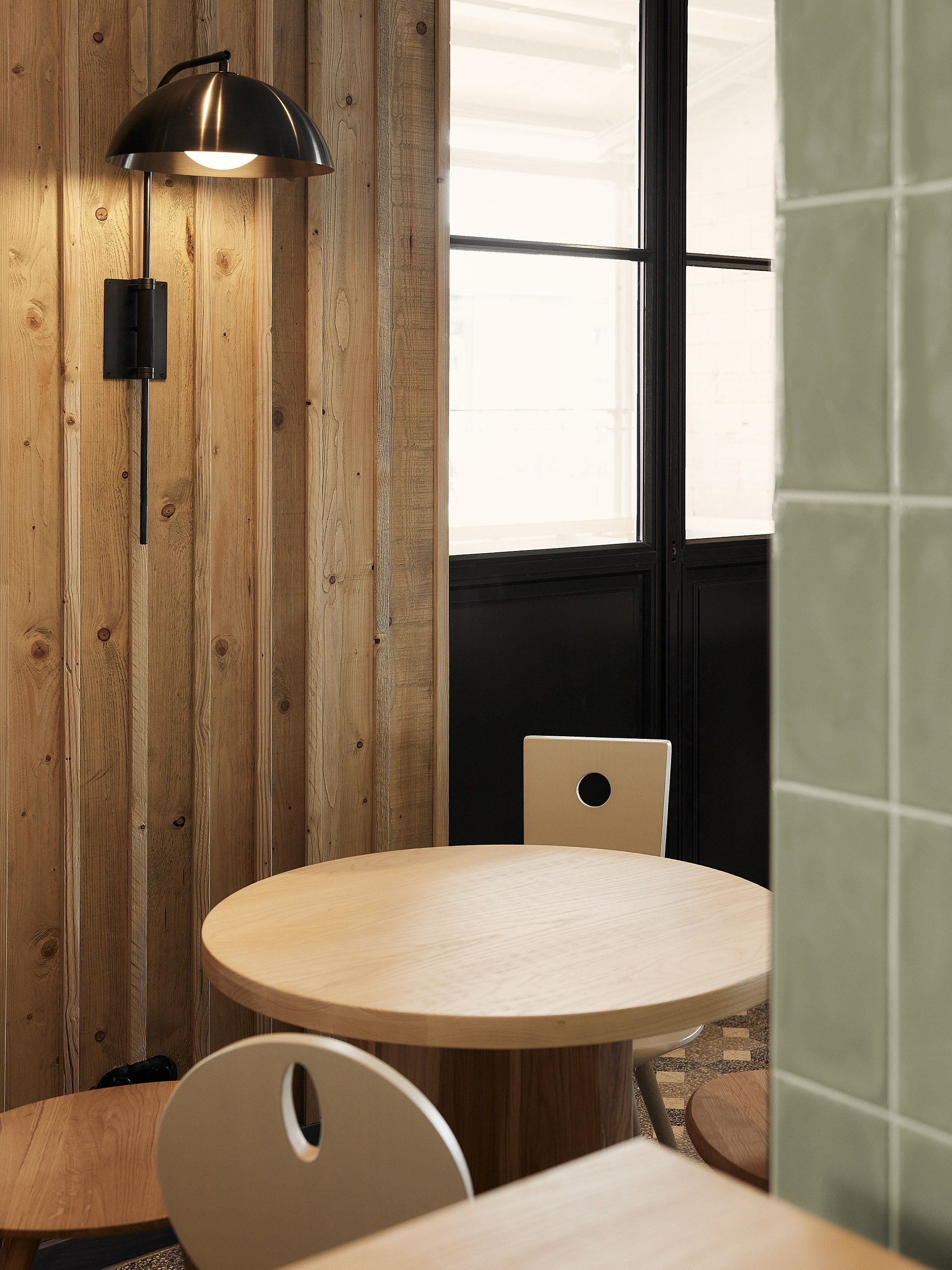 Der runde Holztisch mit schlichten Stühlen und warmer Wandbeleuchte unterstreicht die handwerklich geprägte Innenarchitektur des Benediktiner Weissbräuhauses und schafft eine ruhige, einladende Restaurantatmosphäre.