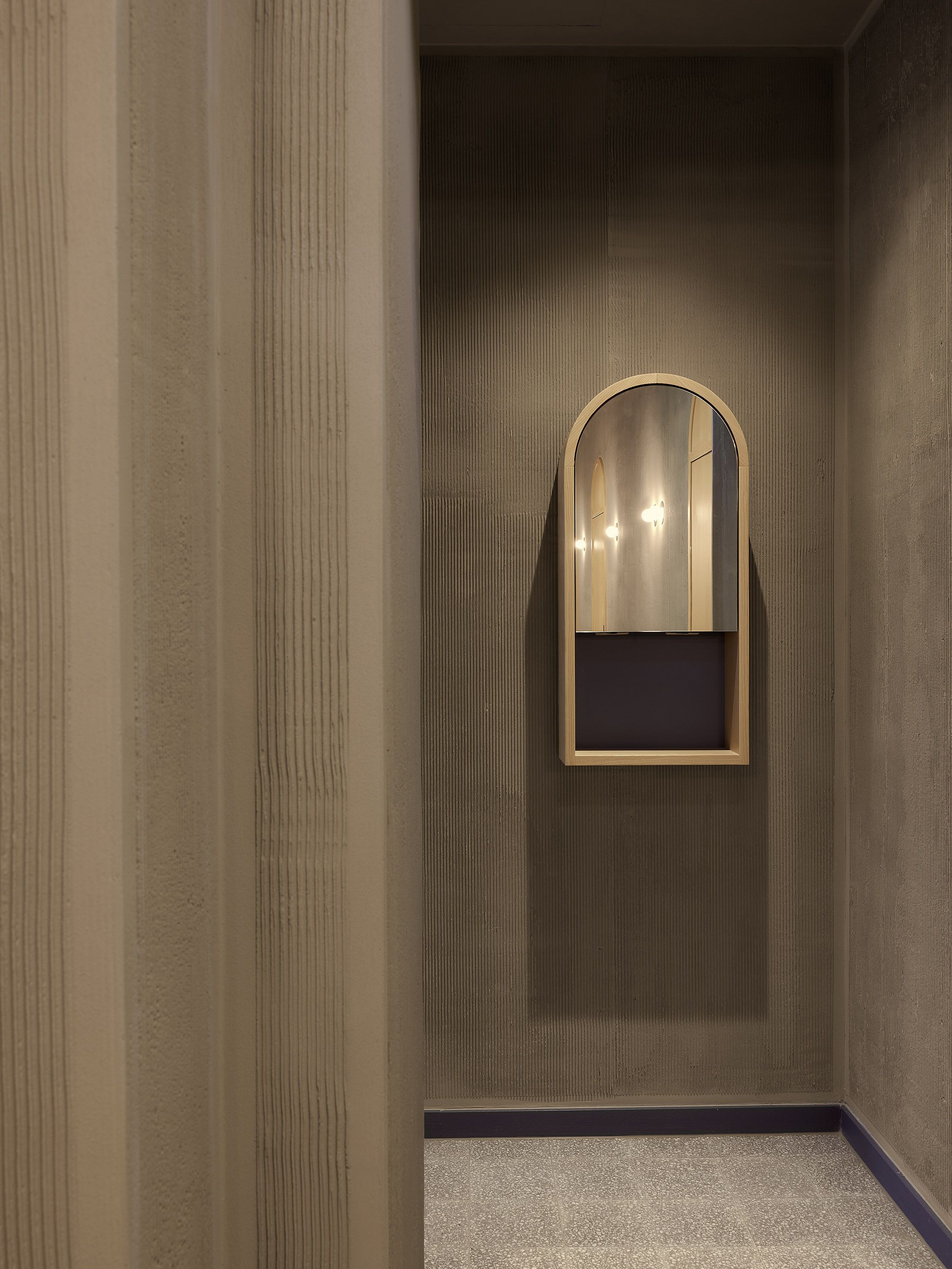 Der reduzierte Flur mit gerillten Wandflächen zeigt die handwerkliche Materialität, die das Interior des Benediktiner Weissbräuhaus definiert.