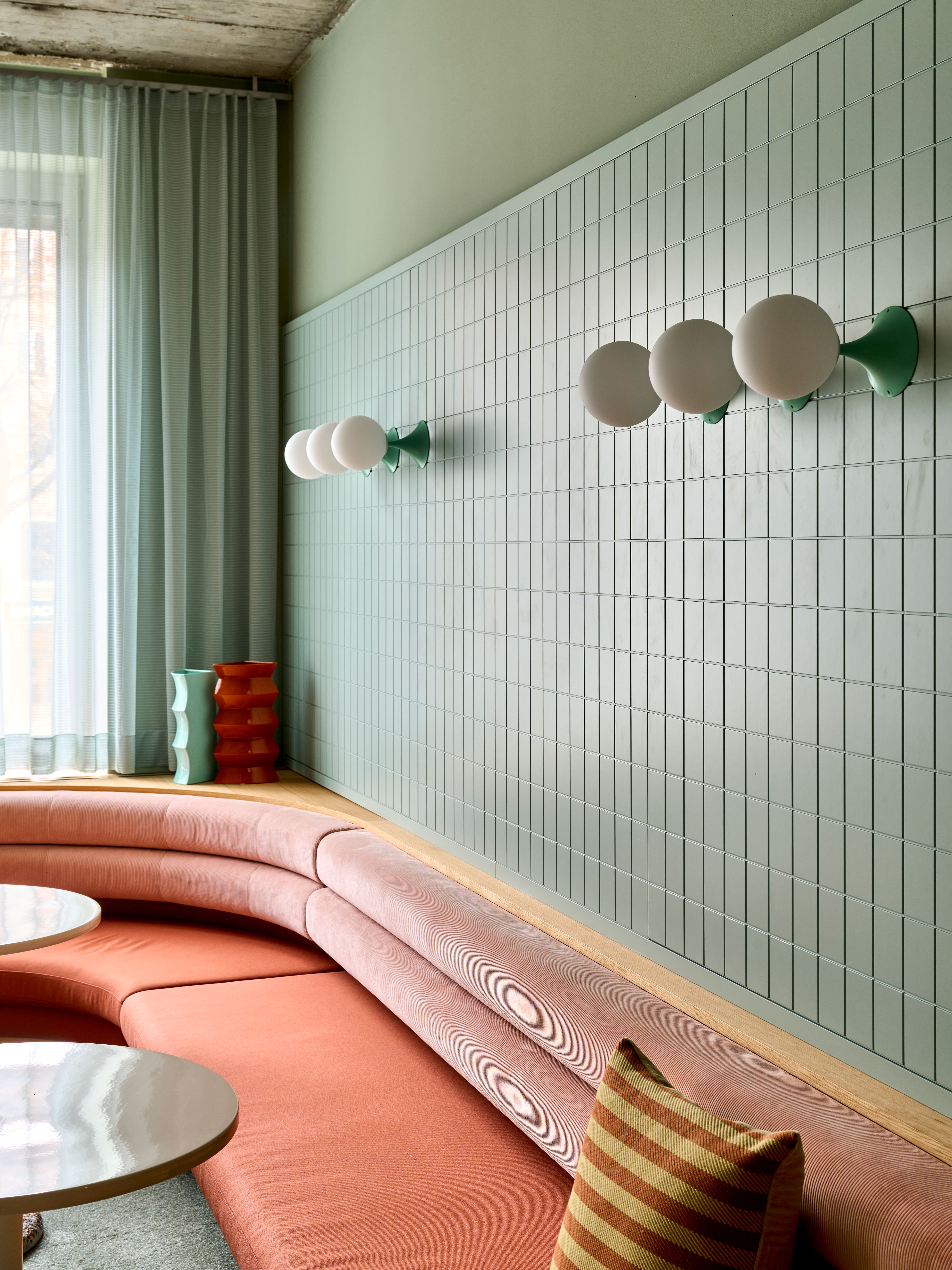 Eine geschwungene Sitzlandschaft in warmem Korallton trifft auf geometrische Fliesen und kunstvolle Wandbeleuchtung als charakteristisches Designmerkmal von Stephanie Thatenhorst.