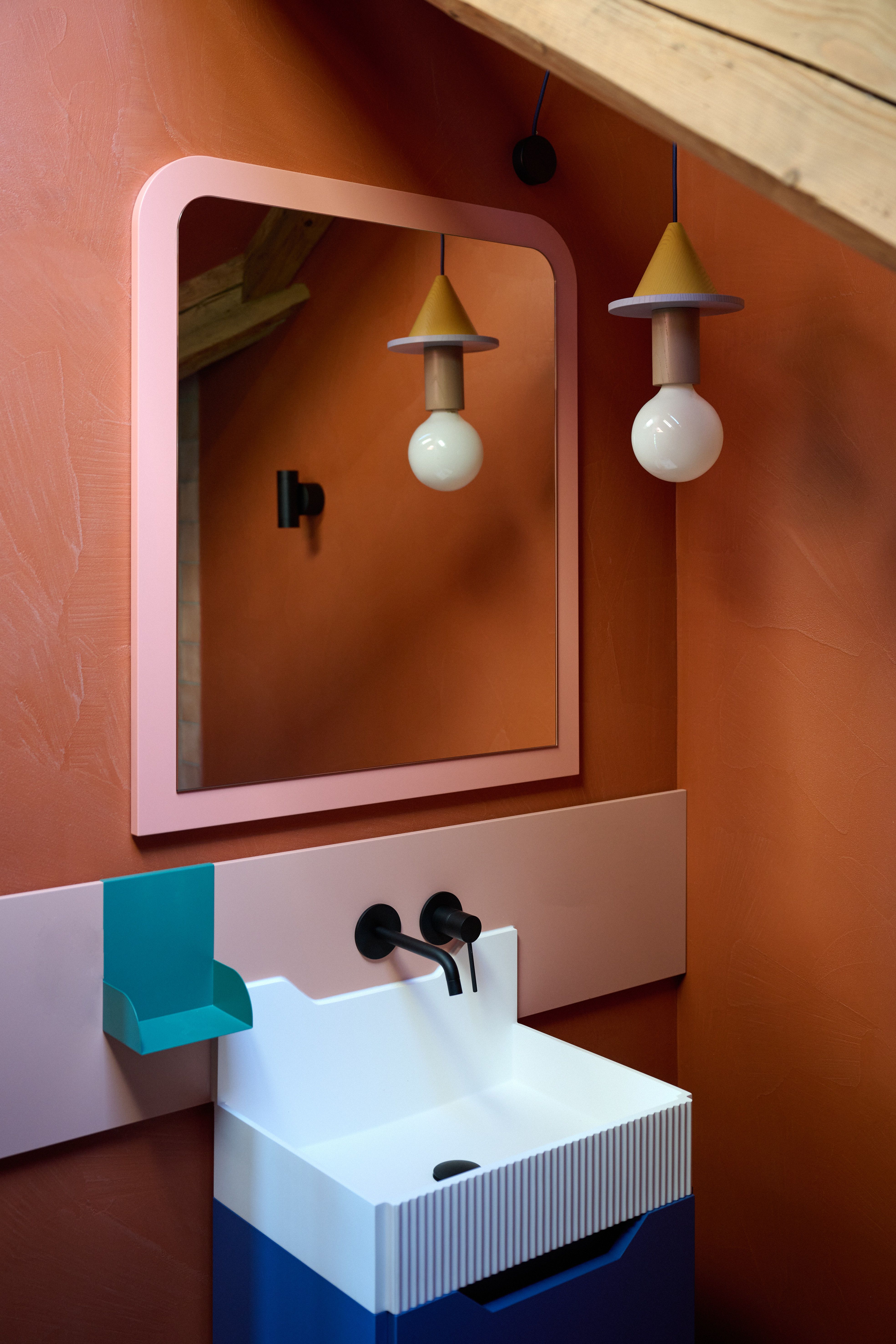 Verspieltes Badezimmerdesign mit farbiger Waschplatz-Inszenierung und geometrischer Leuchte – kuratiert von Stephanie Thatenhorst.