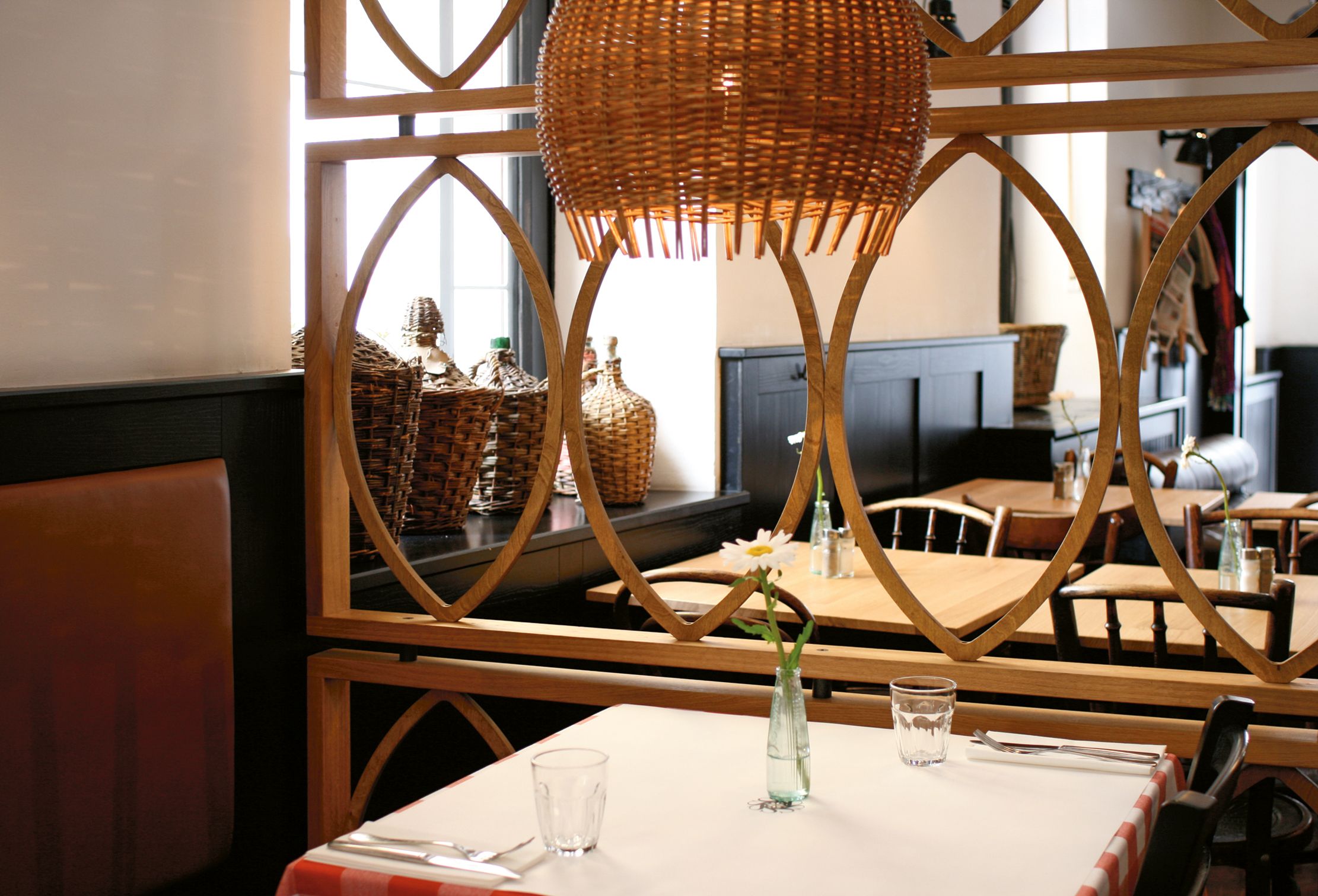 Geflochtene Pendelleuchten und die rhythmische Holzstruktur schaffen eine warme, mediterrane Lichtstimmung im Restaurantinterior.