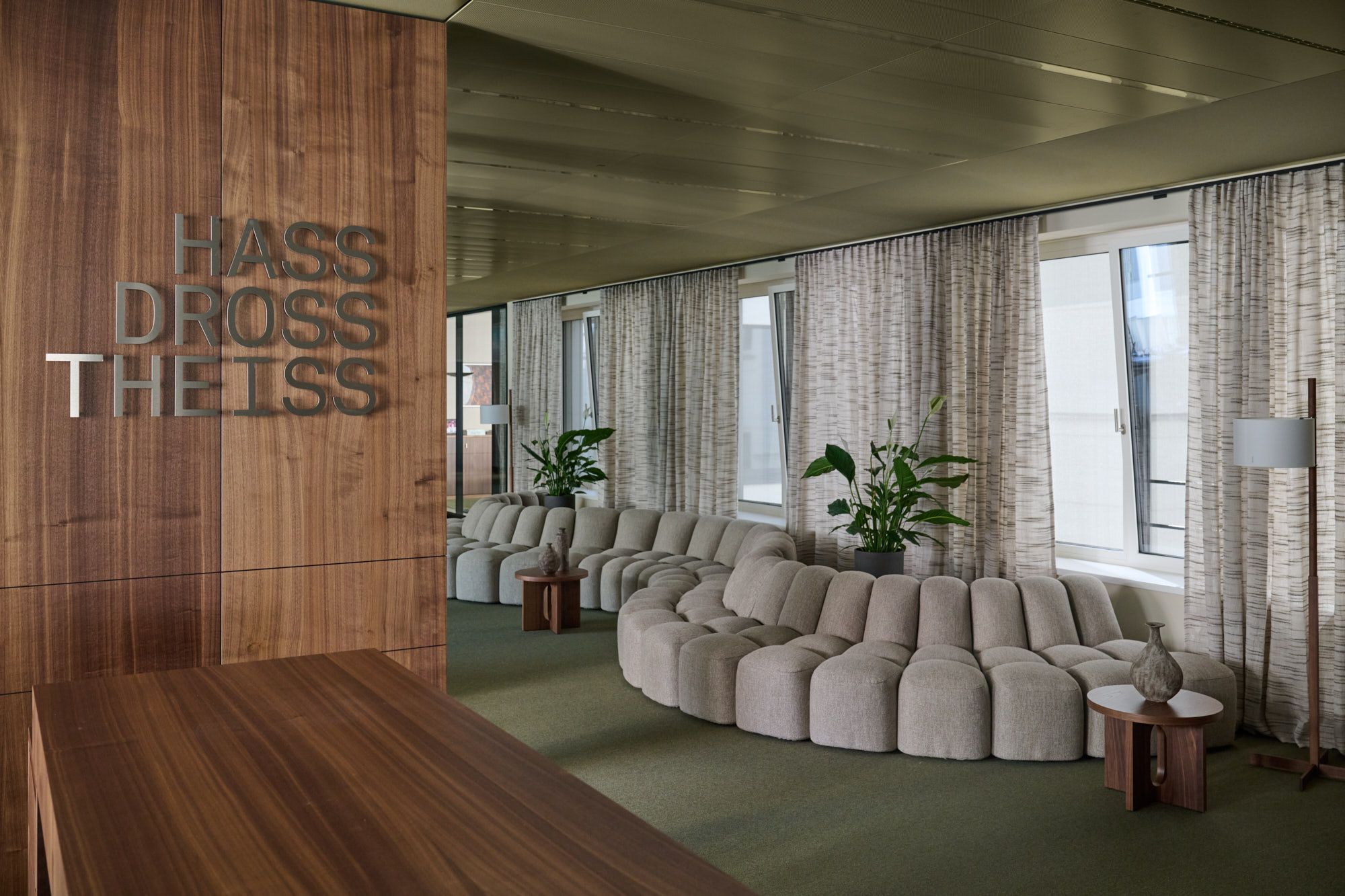 Für das Büro Hass Dross Theiss schafft Stephanie Thatenhorst eine elegante Loungezone, in der warme Holzakzente, skulpturale Polstermöbel und natürliche Texturen eine repräsentative Arbeitsatmosphäre formen.