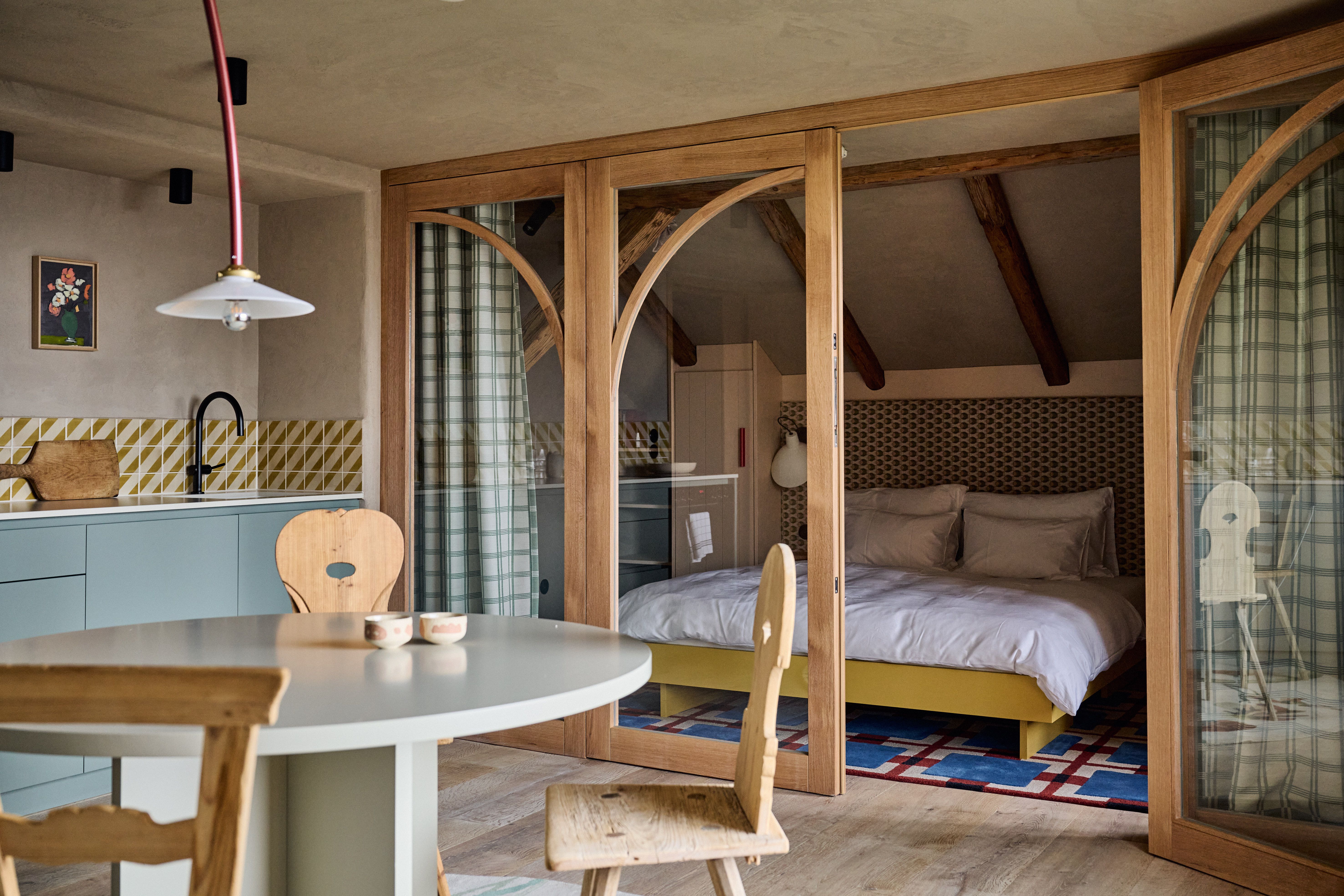 Ein kuratiertes Farmhouse Retreat, designed by Stephanie Thatenhorst, das weiche Pastellküchen, handwerkliche Holzbögen und grafische Textilien zu einer modernen, dennoch ländlich verankerten Wohnatmosphäre verbindet.