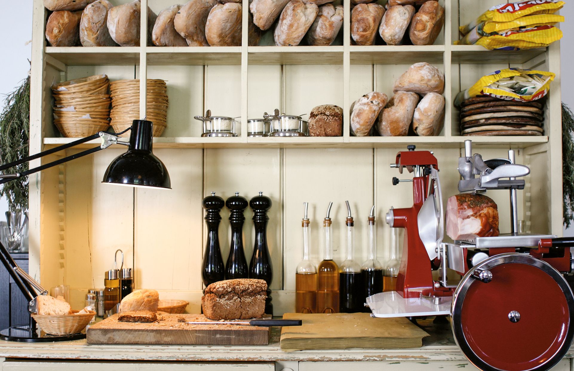 Das offene Regal mit Broten, Ölen und historischen Küchenmaschinen inszeniert Authentizität und handwerkliche Küche als zentrales Gestaltungselement.