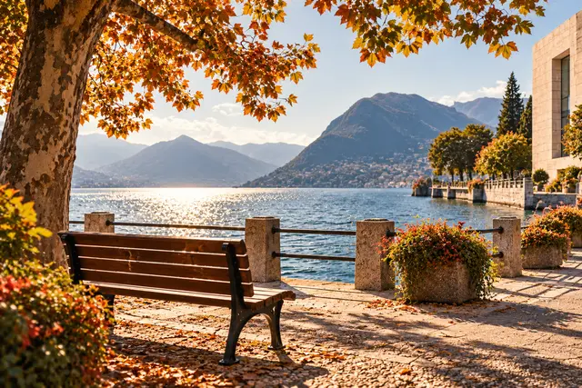 An empty bench overlooks a sunlit lake beneath autumn trees.