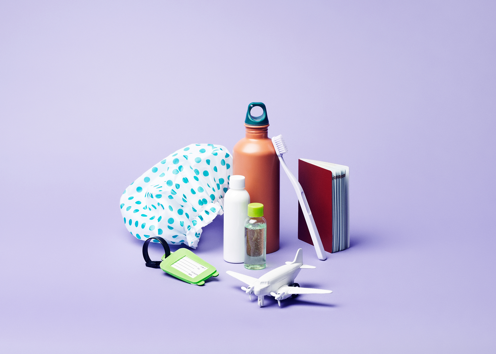 Reiseeffekter som vannflaske, toalettmappe, tannbørste, pass og flymodell mot lilla bakgrunn