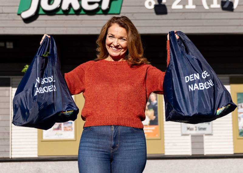 En smilende kunde foran Joker-butikk med fulle handlenett