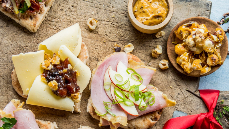 Flatbrød med ulike pålegg – ost med syltetøy og nøtter, skinke med eple og vårløk – servert på en trefjøl