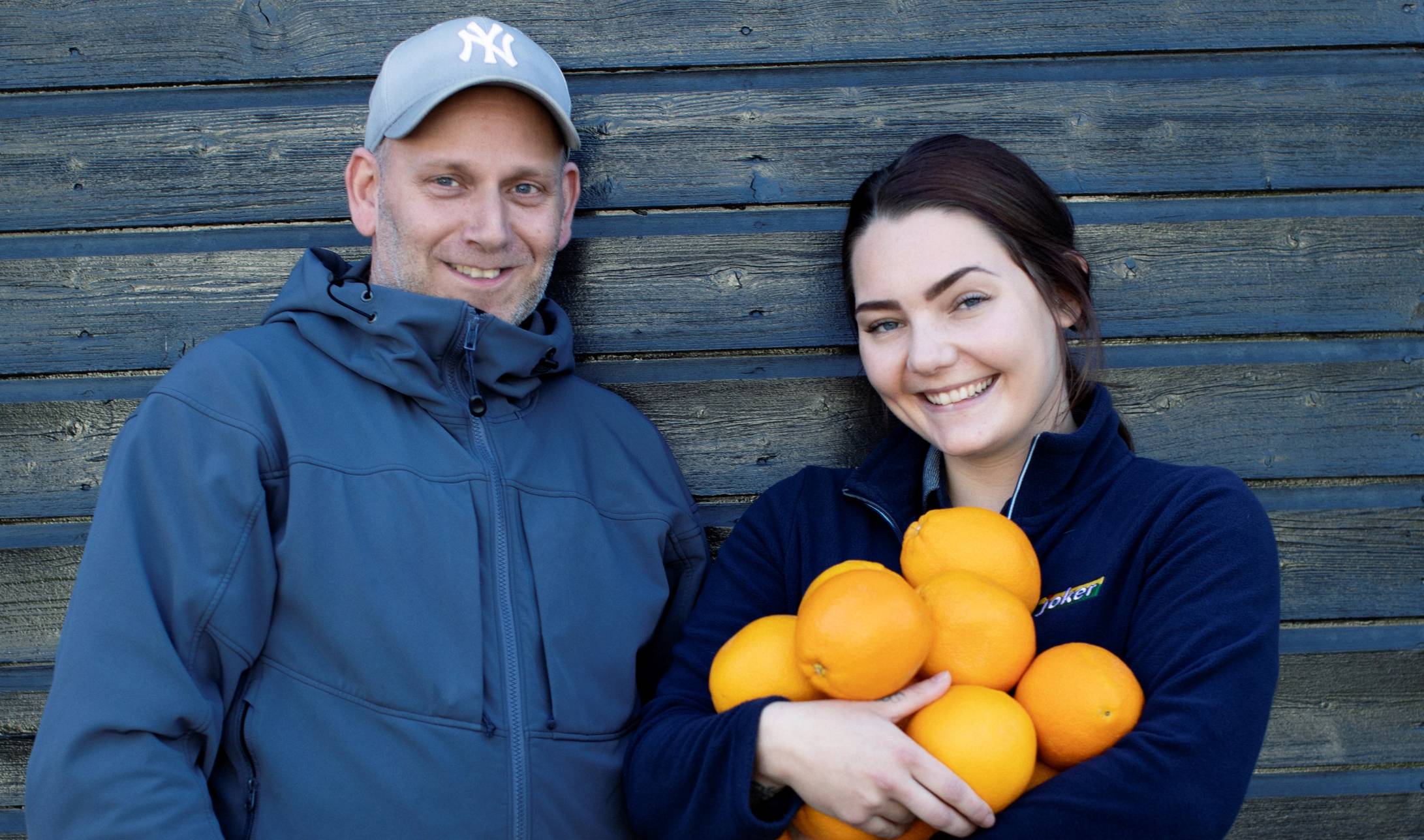 Smilende Joker-ansatt med appelsiner sammen med kunde