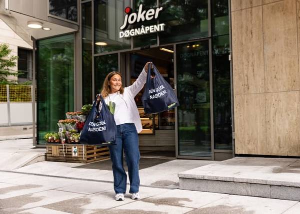 En smilende kvinne utenfor Joker-butikk med handlenett merket Den gode naboen