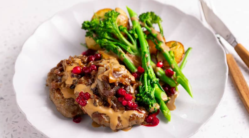 Kjøttkaker med brun saus, tyttebær, stekte poteter og brokkolini servert på hvit tallerken