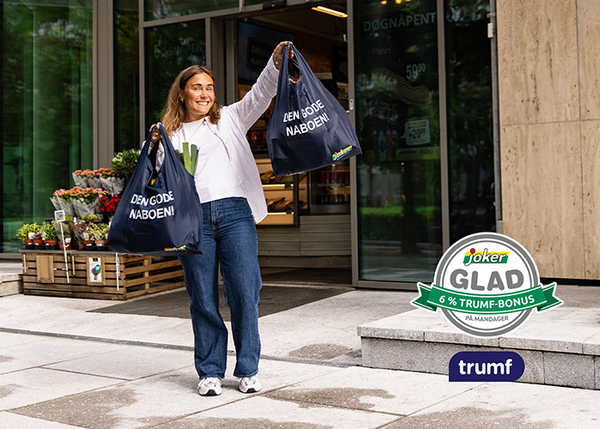 En smilende kvinne utenfor Joker-butikk med handlenett merket Den gode naboen