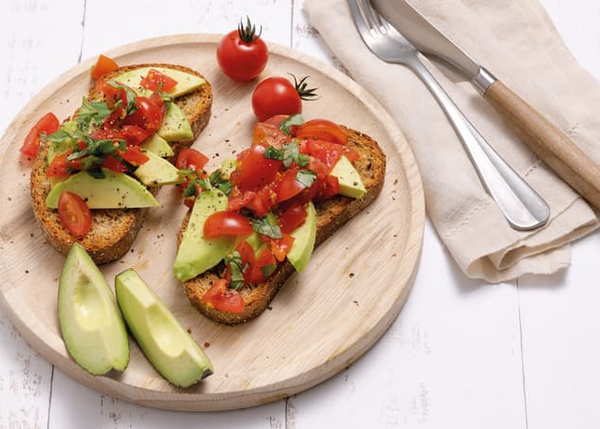 To skiver ristet brød toppet med avocado, cherrytomater og urter