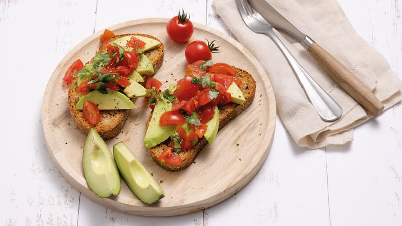 To skiver ristet brød toppet med avocado, cherrytomater og urter