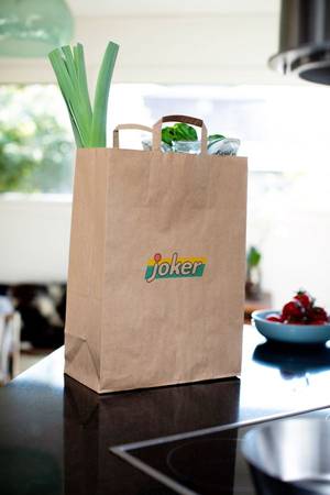 En papirpose med matvarer fra Joker står på en benk