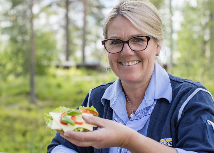 En smilende kvinne i Joker-uniform holder påsmurt brødskive utendørs