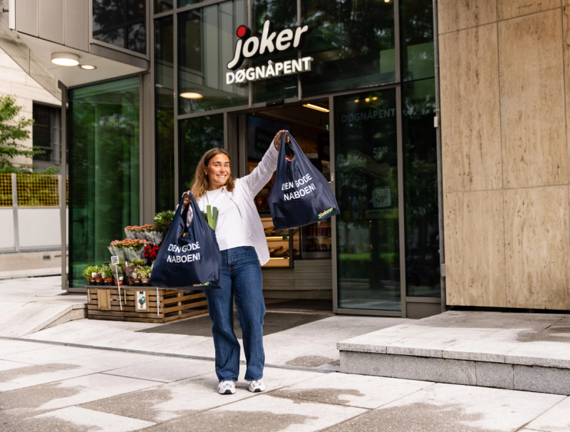 En smilende kvinne med Joker-poser utenfor dagligvarebutikk