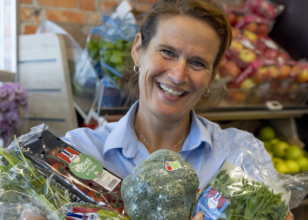 En smilende kvinne i butikk viser frem norske grønnsaker