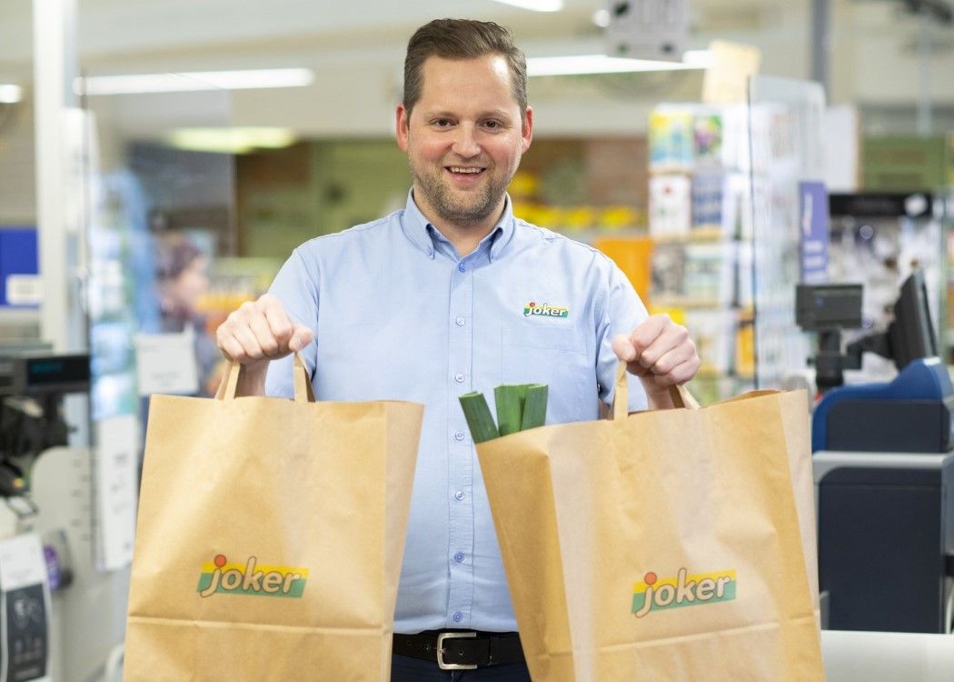 En kjøpmann som står med 2 papirposer fylt med varer