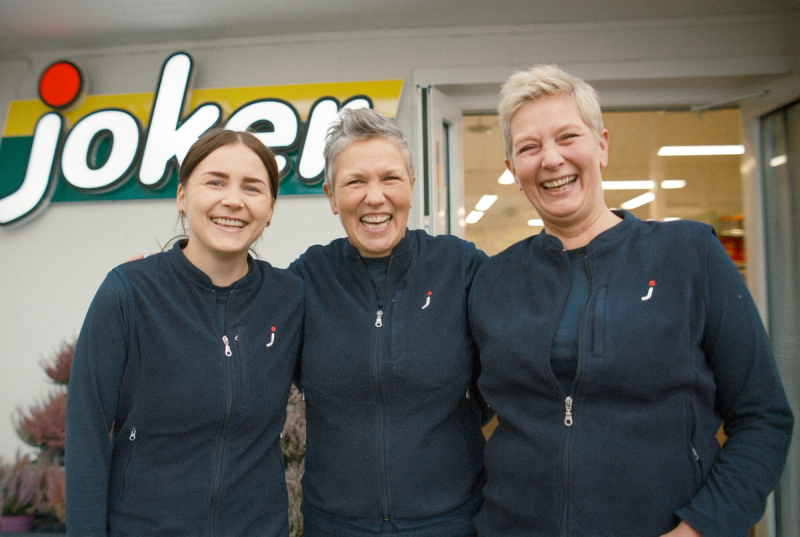 Tre smilende ansatte i Joker-uniform foran butikkens inngang