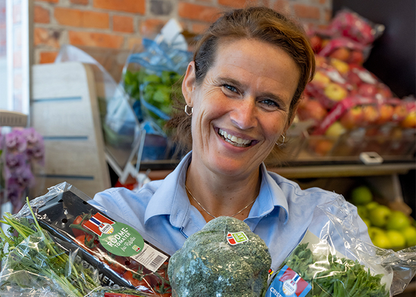 En smilende kvinne viser frem norske grønnsaker
