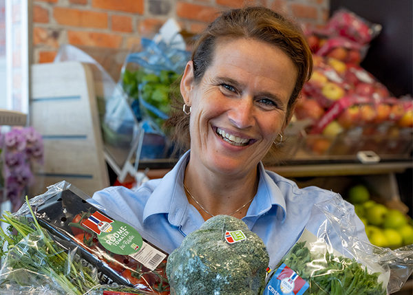 En smilende kvinne viser frem norske grønnsaker
