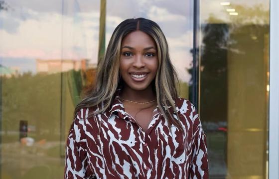 Demi Oloyede in a patterned shirt, standing in front of a glass building with a sunset reflection.