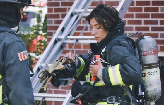 Female firefighter in full gear preparing equipment during a shift, highlighting frontline dedication in a shift-based workforce.