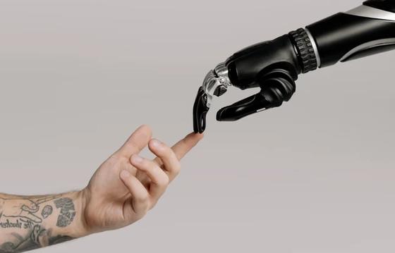 A robotic hand and a human hand reaching out to touch fingertips, symbolizing the connection between AI technology and human collaboration.