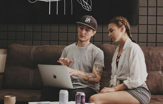 Two colleagues sitting on a couch discussing work while looking at a laptop, fostering collaboration in a casual workplace setting.