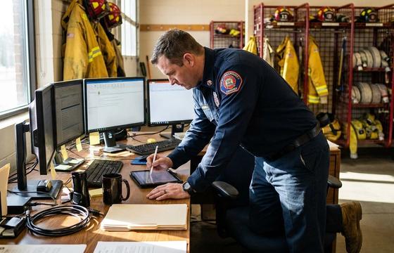Fire officer working across several separate screens at a station desk, illustrating fire department system sprawl