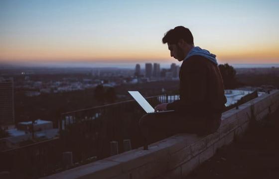 Guy with his laptop outside working, while enjoying the horizon view and weather.