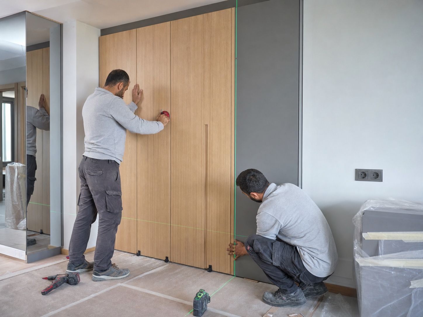 Professional installers aligning full-height oak and grey cabinetry with a laser level