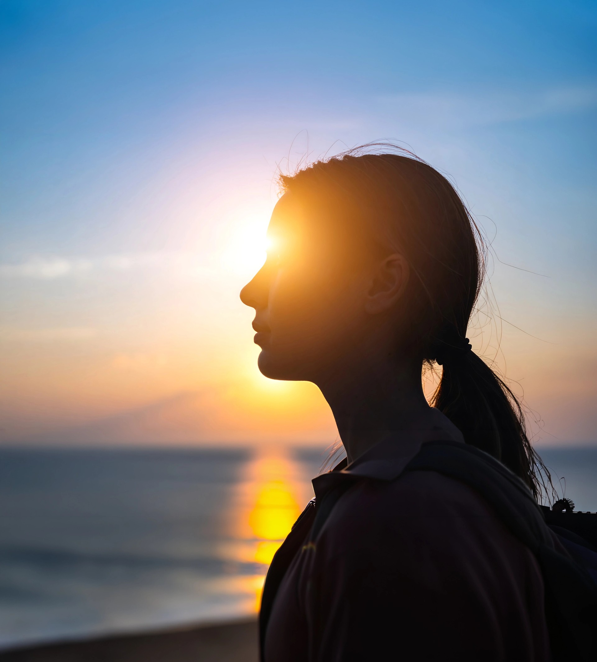 Silhouette of a woman facing the sunrise over the sea