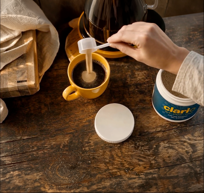 A hand stirring a scoop of Clario powder into a mug of coffee.