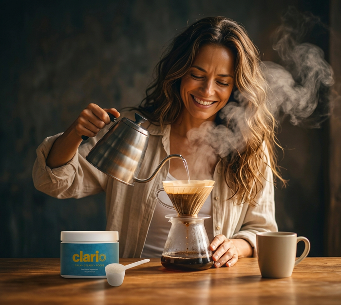 A woman smiling while pouring hot water over a coffee filter, with a container of Clario supplement powder on the table.