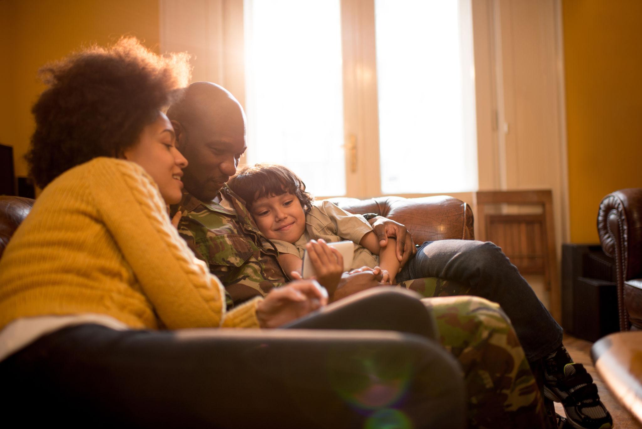 A military-connected family shares a quiet moment at home with their young child while a phone rests face down on a nearby table, emphasizing family privacy over content creation.