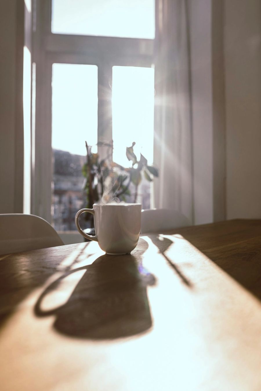 Steaming mug on a wooden table by a sunlit window, a calm start to a morning routine